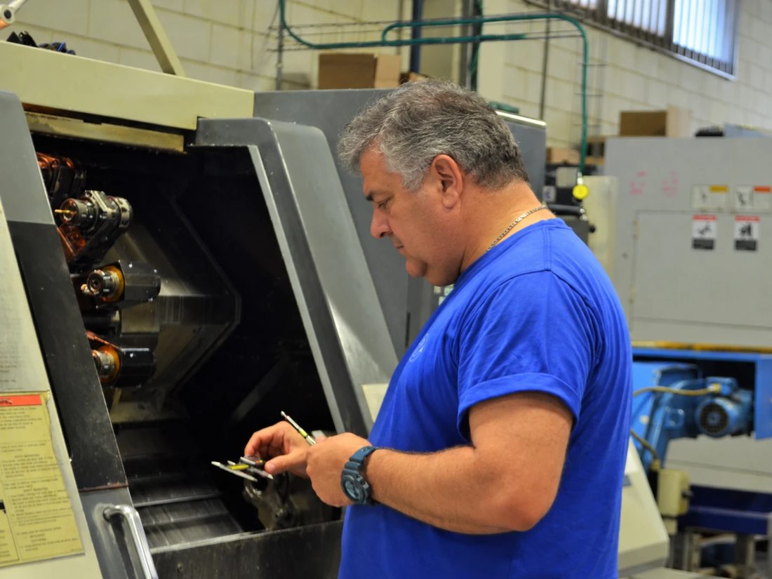 Machinist checking a part with a caliper at a CNC machine